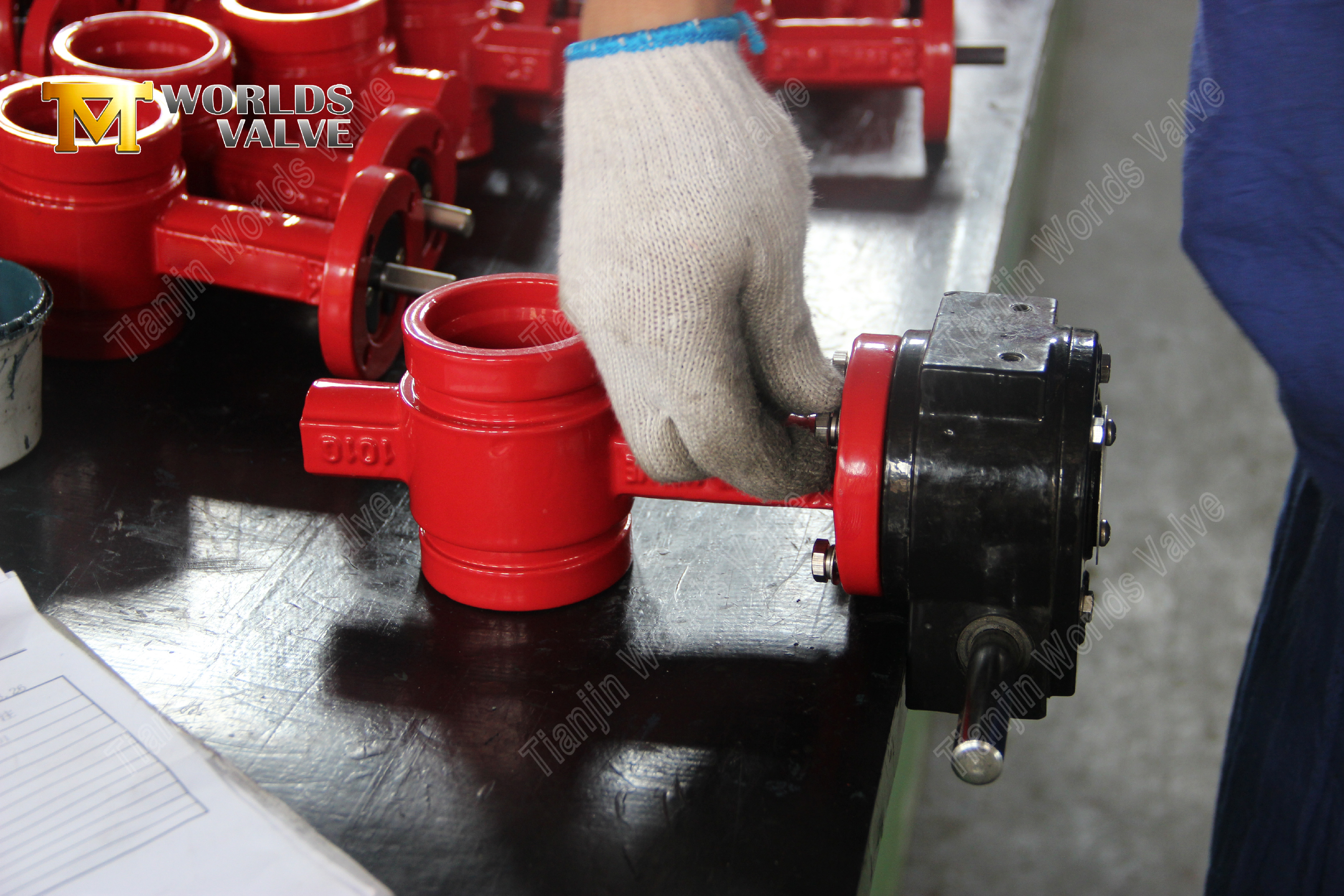 A technician installing a gearbox actuator onto a red grooved butterfly valve